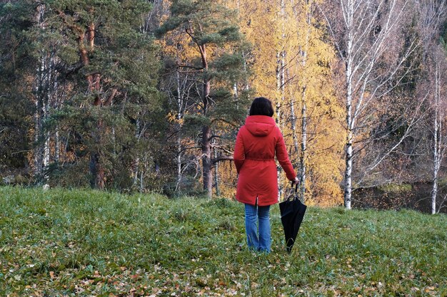 Eine Frau in einer roten Jacke mit Regenschirm spaziert durch den Herbstpark