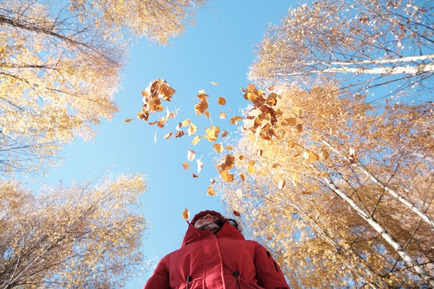 Foto eine frau in einer roten jacke wirft gelbe blätter in die herbstlandschaft