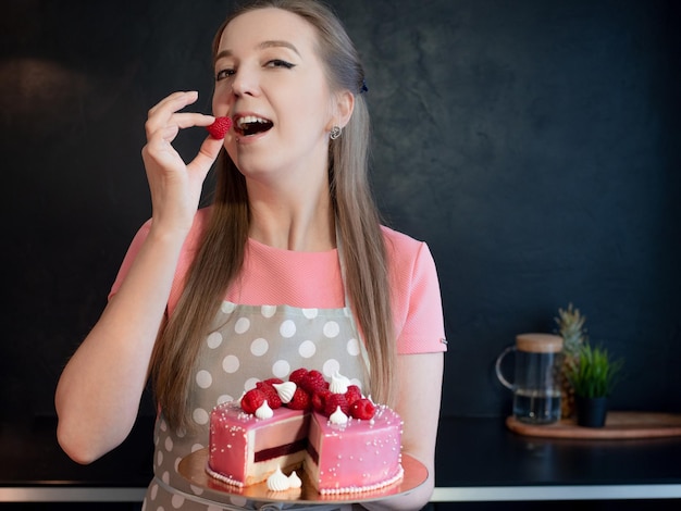 Eine Frau in einer Schürze backt und dekoriert zu Hause einen Kuchen, einen wunderschönen rosa Kuchen mit süßen Himbeeren