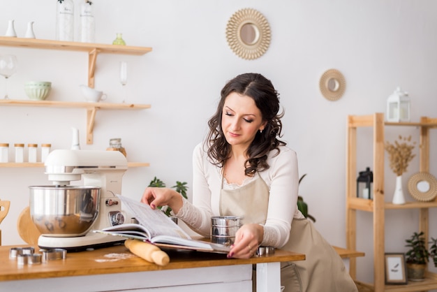 Eine Frau in einer Schürze liest ein Kochbuch. Vorbereitung zum Kochen