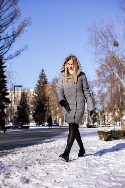 Eine Frau in einer Winter-Daunenjacke und Lederstiefeln geht eine verschneite Straße hinunter Winterschuhe aus Leder für Damen