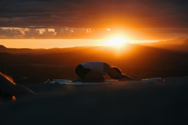 Eine Frau in einer Yoga-Pose macht Yoga vor einem Sonnenuntergang.