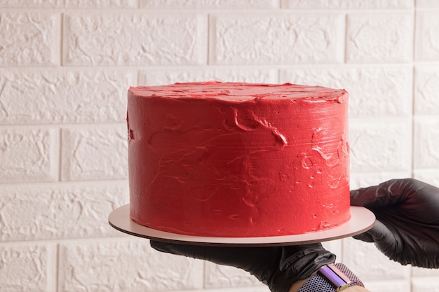 Eine Frau in Handschuhen hält einen Kuchen auf einem Substrat in den Händen