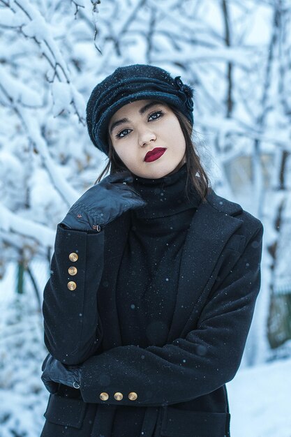 Eine Frau in schwarzem Mantel und Hut steht im Schnee.