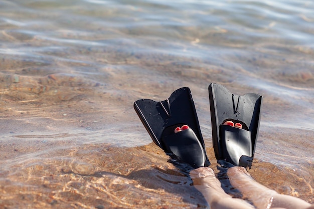 Eine Frau in schwarzen Flossen plantscht in Ufernähe. Flossen ragen aus dem Wasser. Schwimmausrüstung.