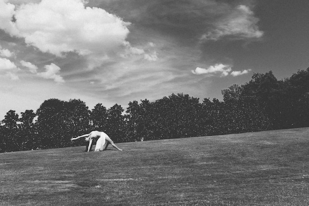 Foto eine frau in voller länge, die sich auf dem feld gegen einen bewölkten himmel ausstreckt