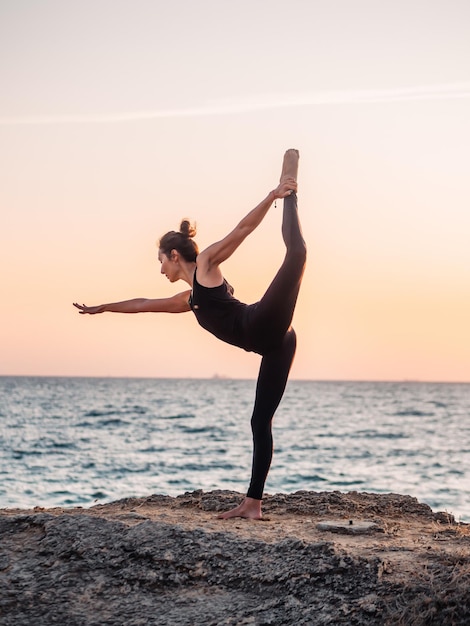 Eine Frau in voller Länge macht Yoga am Strand gegen den Himmel während des Sonnenuntergangs