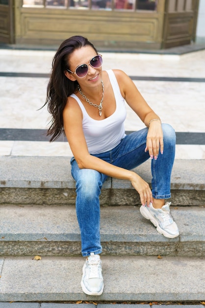 Eine Frau in voller Länge mit Sonnenbrille sitzt auf einer Treppe