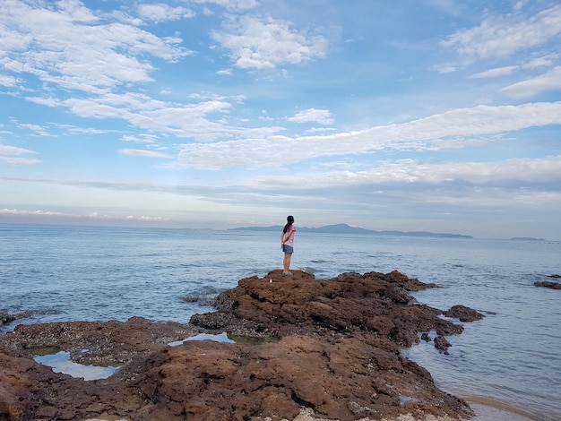 Eine Frau in voller Länge steht auf einem Felsen am Meer gegen den Himmel
