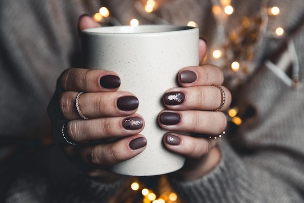 Eine Frau in warmer Kleidung in neutralen Tönen mit einer Weihnachtsgirlande. matte stilvolle Maniküre. Gelpoliermittel.