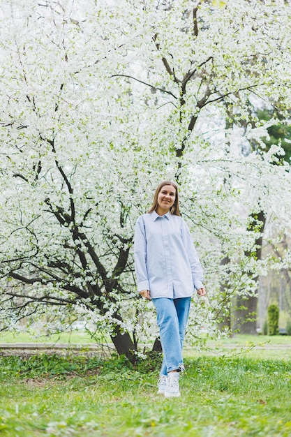 Eine Frau in weißem Hemd und Jeans mit Brille in den Händen in einem Frühlingsgarten