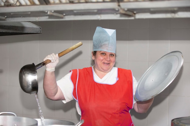 Eine Frau kocht in einer Industrieküche mit einer großen Kelle zwischen Metallpfannen Chef im Krankenhaus