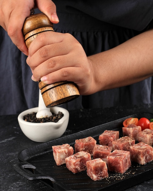 Eine Frau kocht mit Paprika frische rohe Saikoro gewürfelte Steaks aus marmoriertem japanischem Rindfleisch auf dunklem Hintergrund.