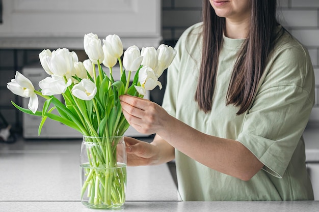 Eine Frau legt ein Bouquet weißer Tulpenblumen in eine Vase in der Küche