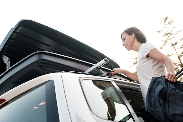 Eine Frau legt vor einem Familienausflug in den Urlaub Dinge in den Dachgepäckträger eines Autos oder in eine Frachtbox