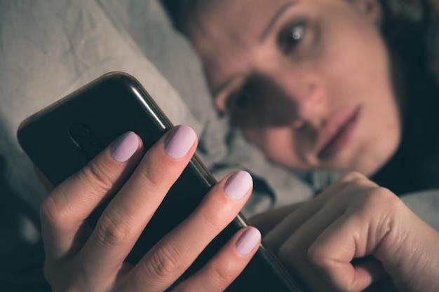 Eine Frau liegt im Bett und benutzt ein Smartphone