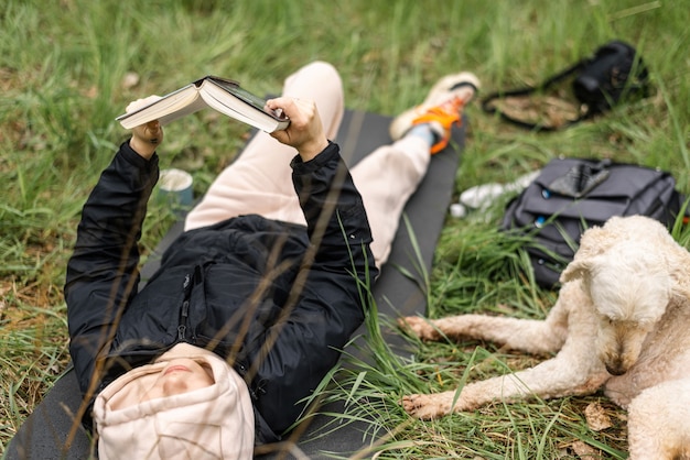 Foto eine frau liegt im gras und liest ein buch. ein hund ruht in der nähe. camping, entspannung.