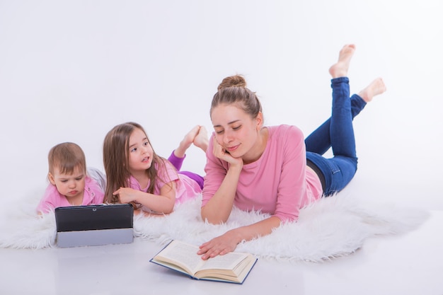 Eine Frau liest ein Buch, Kinder schauen sich einen Cartoon auf einem Tablet an. Hobbys und Erholung mit Gadgets. Familienurlaub, Zeit miteinander verbringen. Heimunterricht