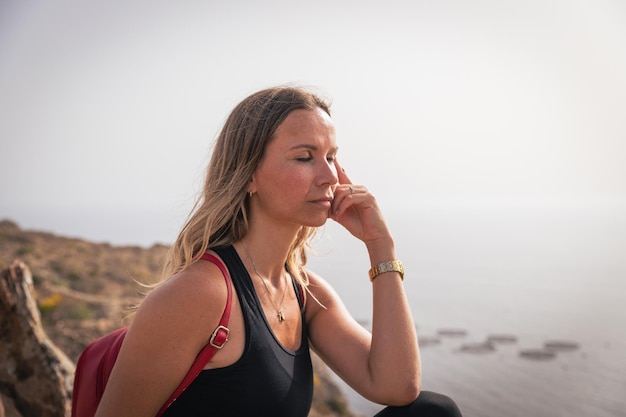 Eine Frau macht beim Wandern eine Pause und meditiert auf einem Felsen sitzend