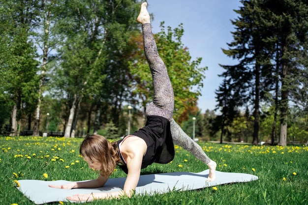 Eine Frau macht ein Yoga-Asana-Pose-Workout im Park Harmonie und Gleichgewicht des Körpers verwendet eine Matte