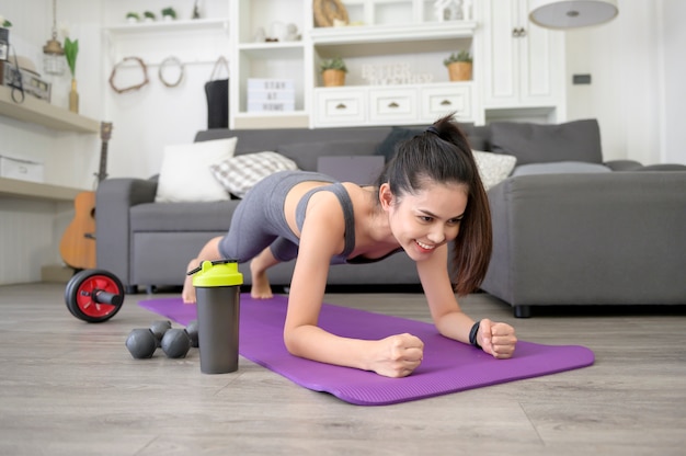 Eine Frau macht Yoga-Planke und sieht Online-Trainings-Tutorials auf ihrem Laptop im Wohnzimmer, Fitness-Training zu Hause, Gesundheitstechnologie-Konzept.