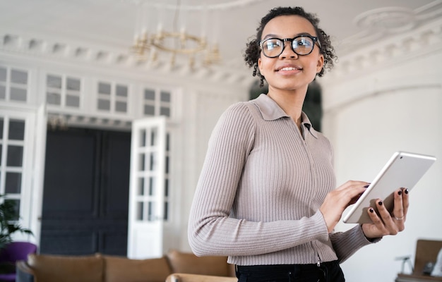 Eine Frau mit Brille arbeitet am Arbeitsplatz eines Finanzunternehmens im Büro und nutzt ein Tablet und das Internet