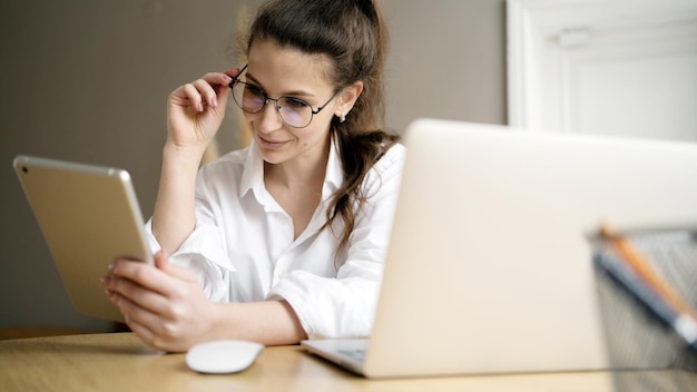 Eine Frau mit Brille ist eine Freiberuflerin, die in einem Büro mit einem Laptop arbeitet und einen Projektbericht erstellt