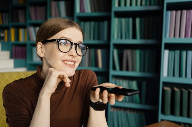 Eine Frau mit Brille nimmt eine Audionachricht auf und arbeitet mit einem Telefon in einem Büro in einem Coworking Space