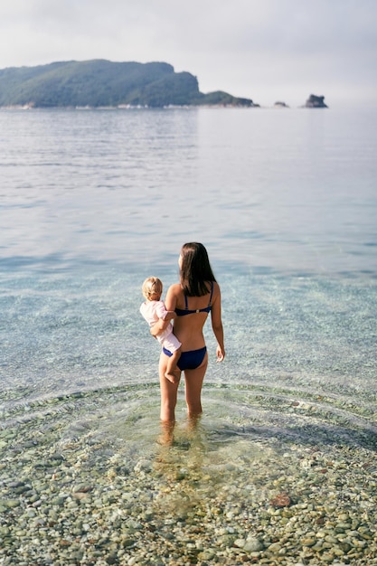 eine Frau mit einem Baby auf dem Rücken hält ein Baby im Wasser.