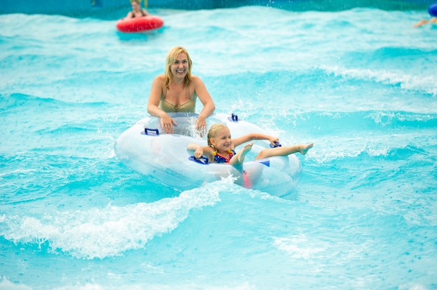 Eine Frau mit einem Kind in einem aufblasbaren Gummikreis spielt im Regen im Pool eines Sommerwasserparks.