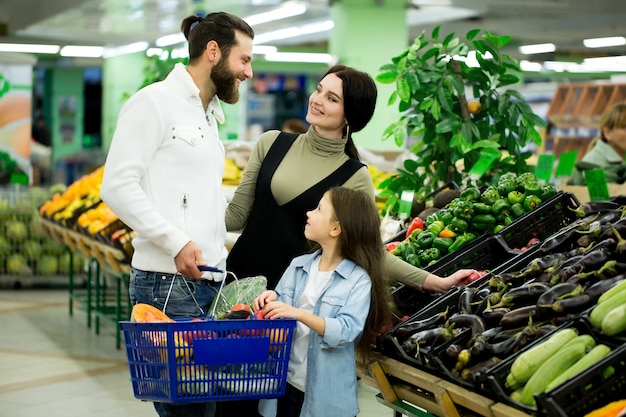 Eine Frau mit einem Mann und einem Kind, die Gemüse beim Einkaufen in einem Gemüsesupermarkt auswählen