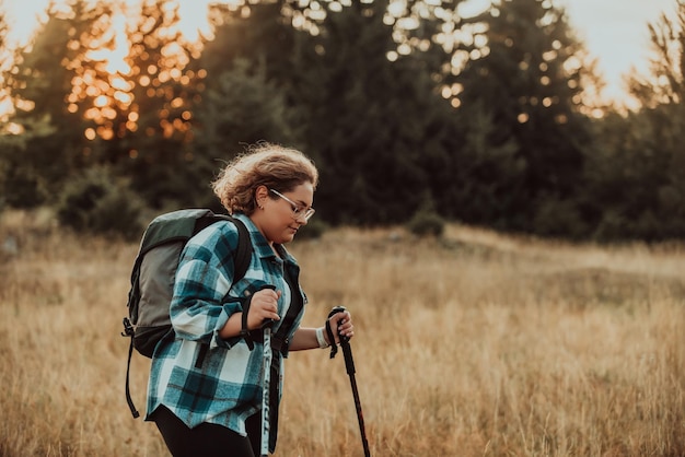 Eine Frau mit einem Rucksack auf dem Rücken und Bergsteigerausrüstung, die bei Sonnenuntergang auf einem Berg spazieren geht