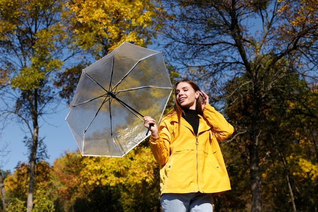 Eine Frau mit einem transparenten Regenschirm lächelt vor herbstgelben Bäumen an einem sonnigen Tag Herbststimmung