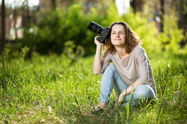 Eine Frau mit einer Kamera, die auf dem Gras im Park sitzt