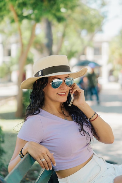 Foto eine frau mit hut und sonnenbrille telefoniert, während sie einen hut trägt.