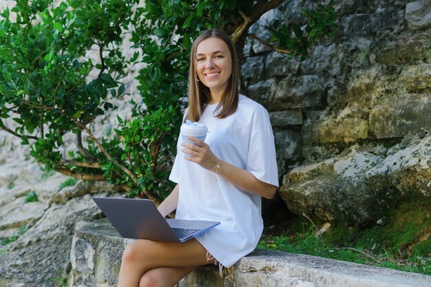 Eine Frau mit Kaffee und einem Laptop auf dem entspannten Leben des Hipster-Lebensstils im Freien