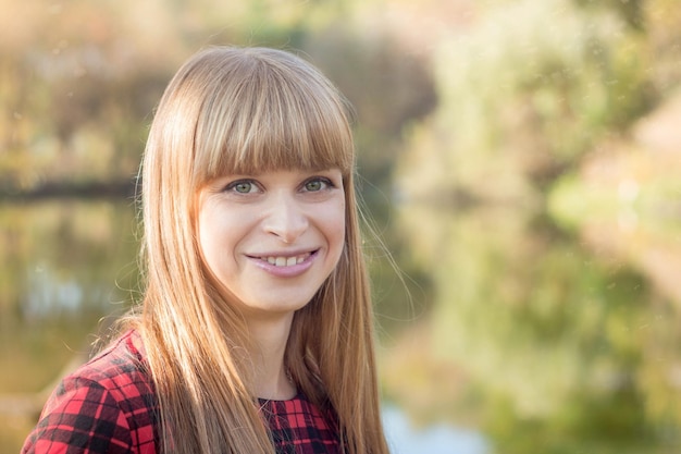 Eine Frau mit langen blonden Haaren lächelt vor einem See.