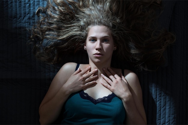 Eine Frau mit langen blonden Haaren liegt auf einem Bett mit einer blauen Decke.