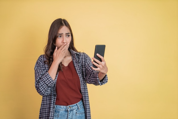 Eine Frau mit langen Haaren, die ein Handy benutzt, ist überrascht, einen Handybildschirm mit Exemplar zu sehen