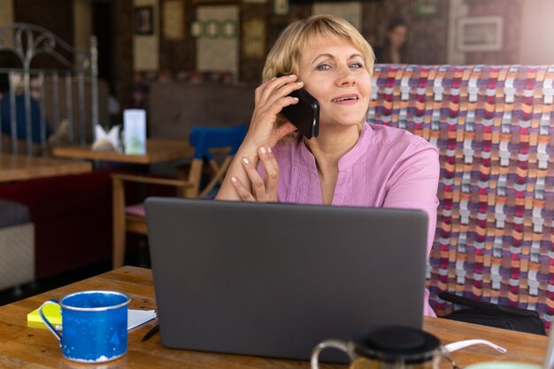 Eine Frau mit Laptop arbeitet in einem Büro. Eine Geschäftsfrau mittleren Alters sitzt in einem Café. Sie spricht auf ihrem Smartphone.