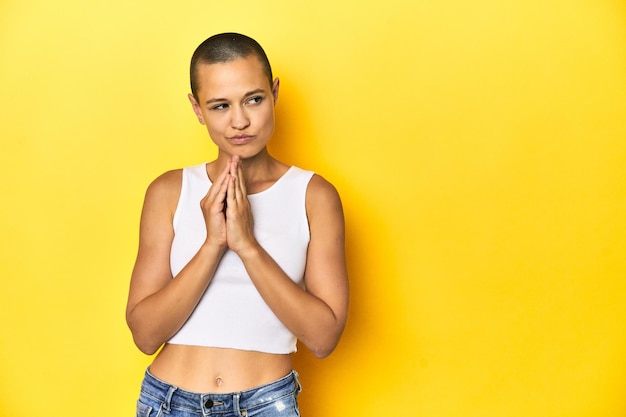 Eine Frau mit rasiertem Kopf in weißem Tanktop und gelbem Hintergrund schmiedet im Kopf einen Plan und schmiedet eine Idee