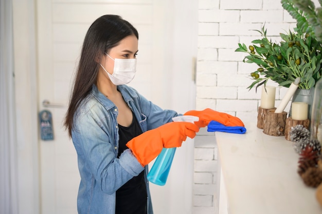 Eine Frau mit Reinigungshandschuhen unter Verwendung von Alkoholspray-Desinfektionsmittel zur Reinigung des Hauses, gesund und medizinisch, Covid-19-Schutz zu Hause Konzept.