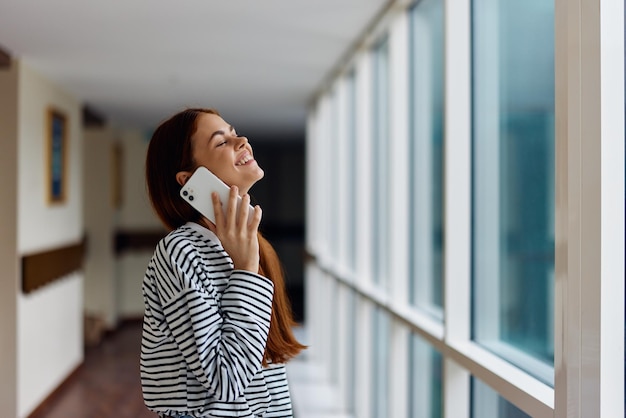 Eine Frau mit roten Haaren und einem Telefon in der Hand redet und lacht, während sie aus dem Fenster auf die Stadt blickt