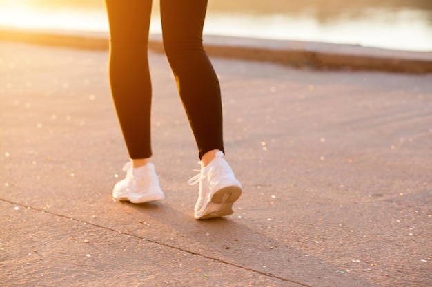 Eine Frau mit schlanker, muskulöser Figur läuft in schwarzer Sportkleidung und weißen Turnschuhen in der Natur herum. Zugeschnittene Fotos. junge Fitnessfrau