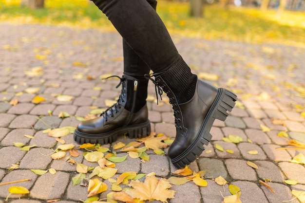 Eine Frau mit schwarzen Stiefeln steht auf einem Ziegelsteinweg im Herbstlaub.