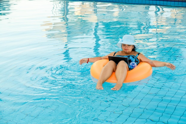 Eine Frau mit Sonnenhut im Pool im Schwimmkreis mit Laptop kommuniziert per Videoschaltung