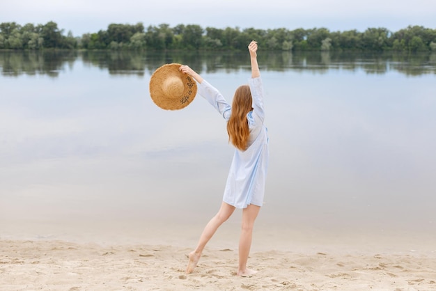 Eine Frau mit Strohhut am Strand genießt das Leben rückwärts