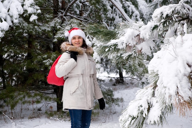 Eine Frau mit Weihnachtsmütze geht in einem schneebedeckten Kiefernwald spazieren