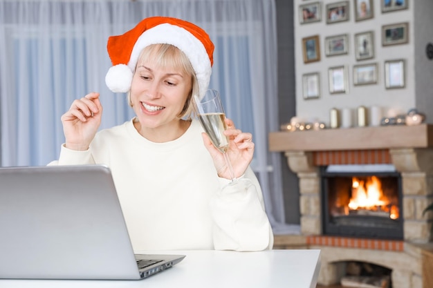 Eine Frau mit Weihnachtsmütze hält ein Glas Champagner Verwandte und Freunde auf einem Laptop zu Weihnachten