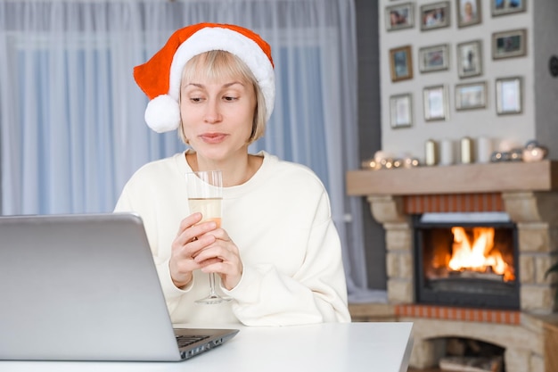 Eine Frau mit Weihnachtsmütze hält ein Glas Champagner Verwandte und Freunde auf einem Laptop zu Weihnachten